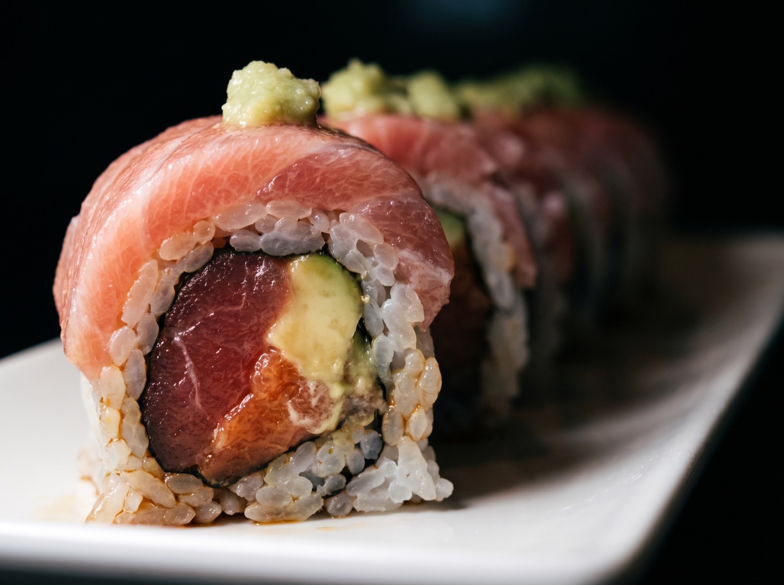 A row of tuna-topped rolls with wasabi, on a white plate at the Hikari sushi bar.