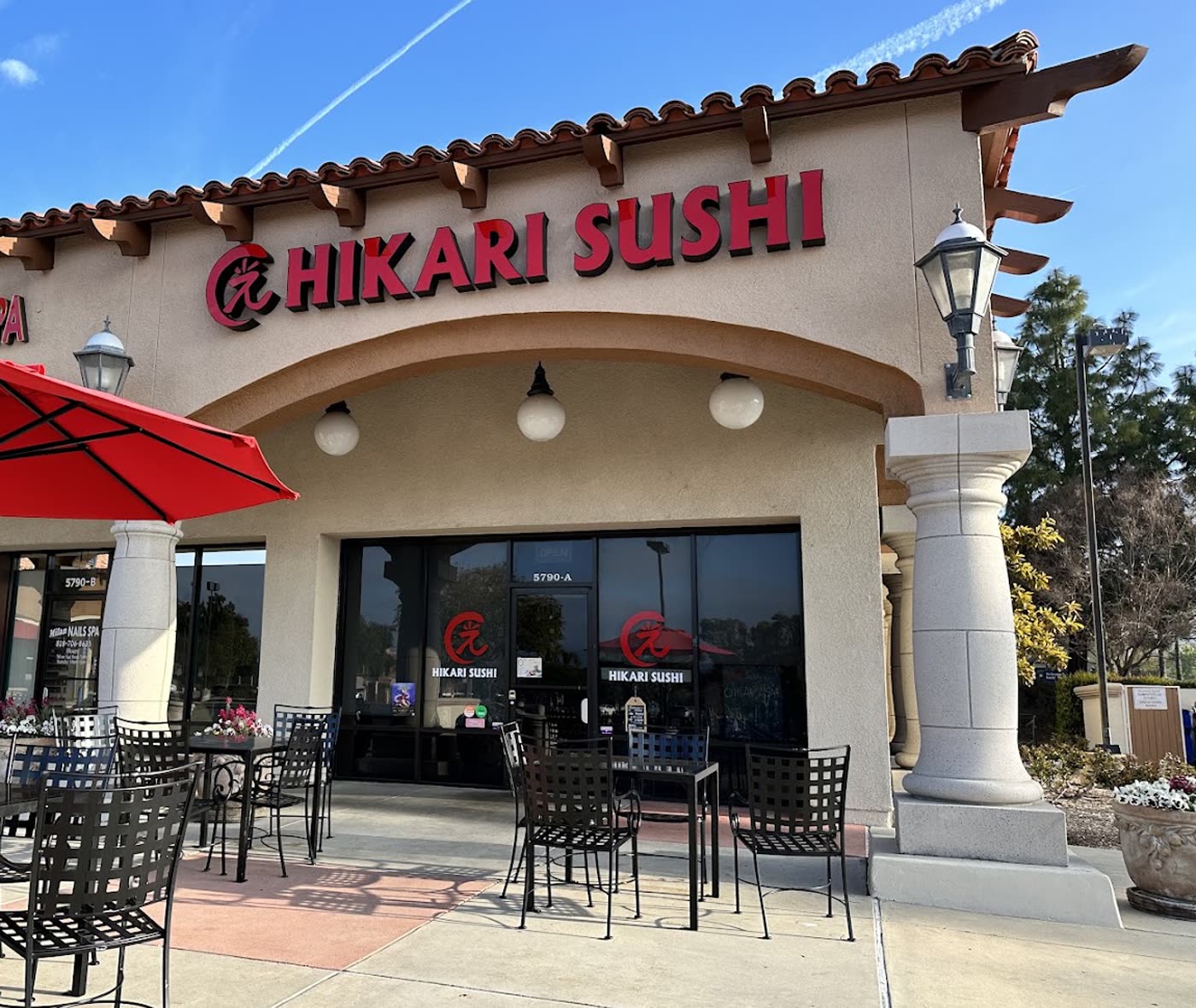 The Hikari Sushi storefront at 5790 Lindero Canyon Rd: red sign over an arched entry, patio tables under a red umbrella.